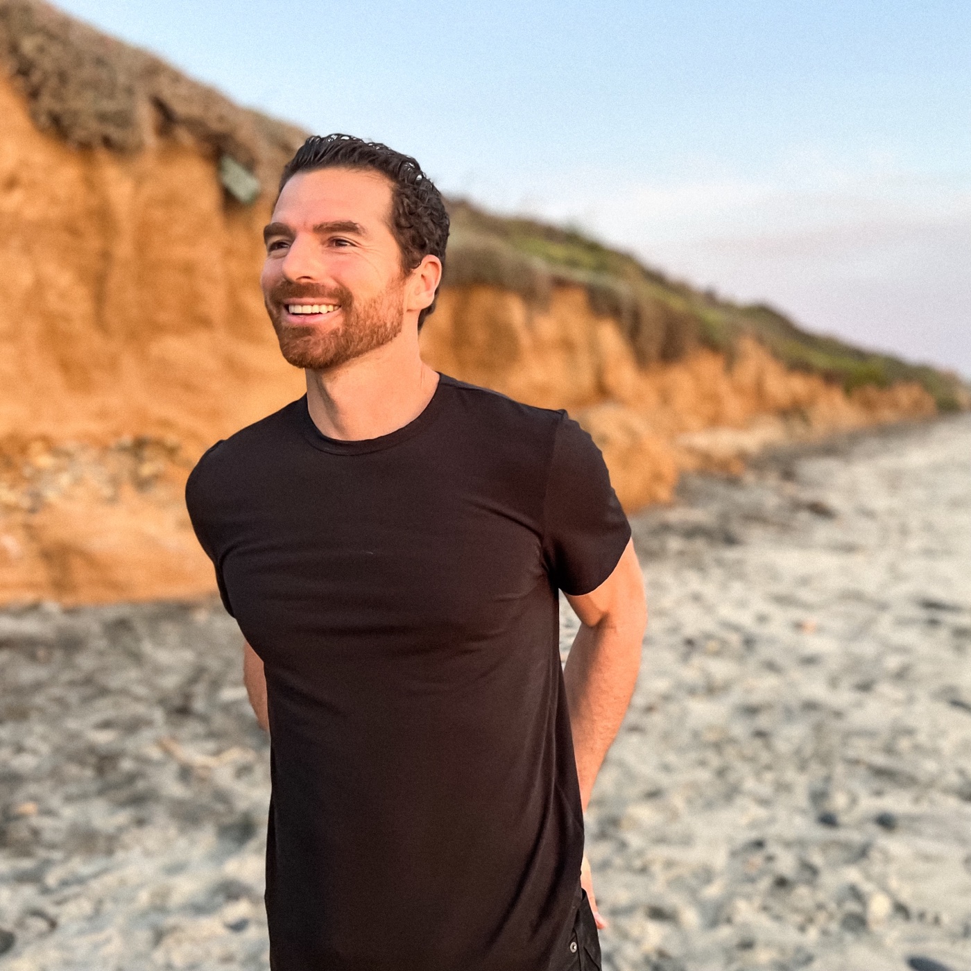 Jared smiling on the beach below golden cliffs
